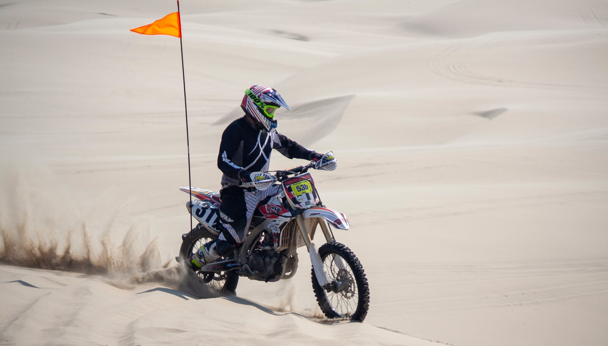 Motocross rider throwing sand on desert dunes